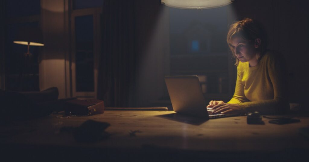 O femeie stă seara la birou și lucrează la laptop