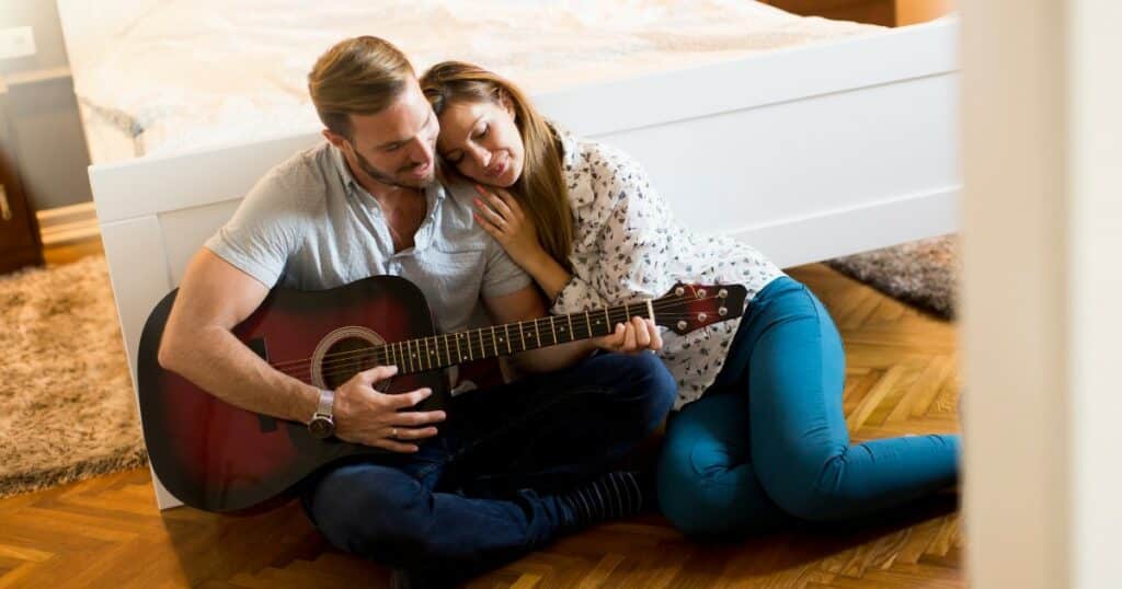 Un barbat cant la chitara si iubita lui in asculta sprijinindu-si capul pe umarul lui