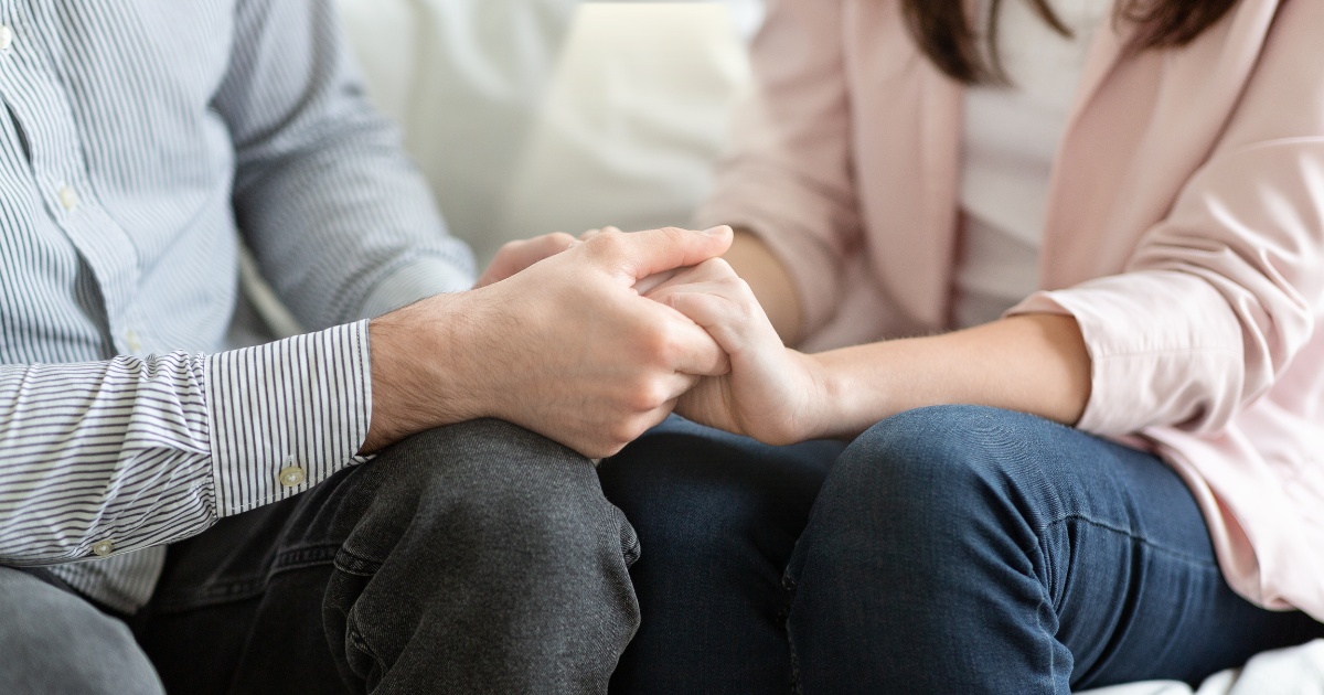Partenerii de cuplu (sotul si sotia) se tin de maini stand pe canapea in cabinetul de psihoterapie