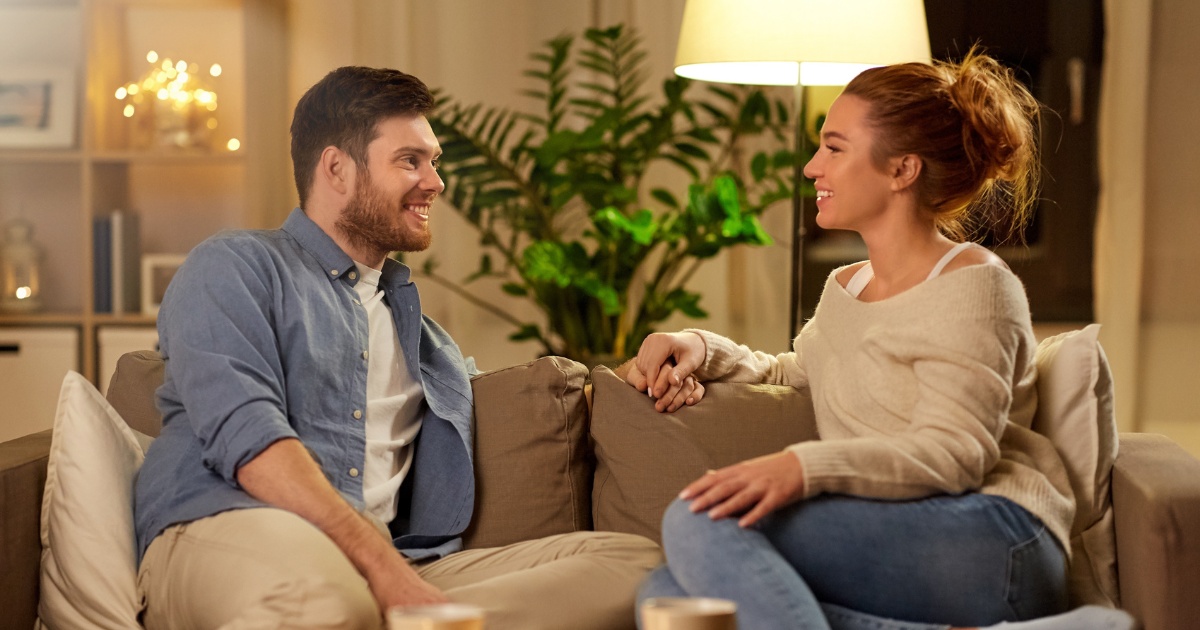 Partners holding hands, discuss sitting on the couch the possibility of seeing a couples psychologist